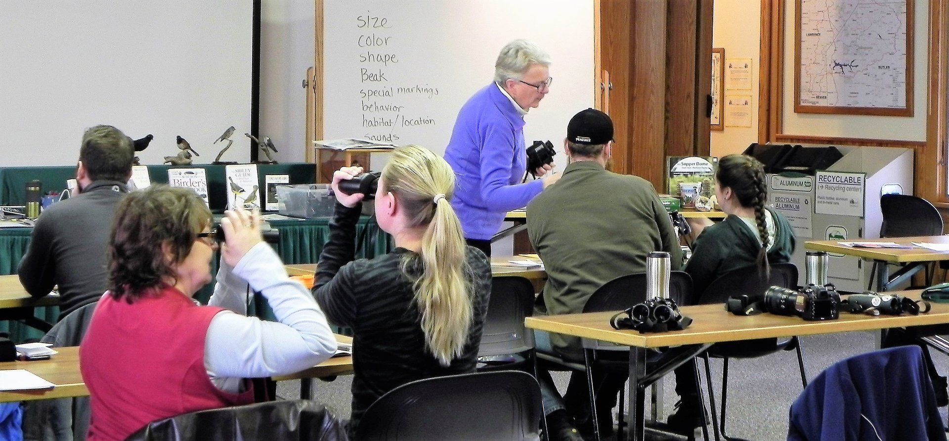 A group of people are sitting at tables with cameras in a room.