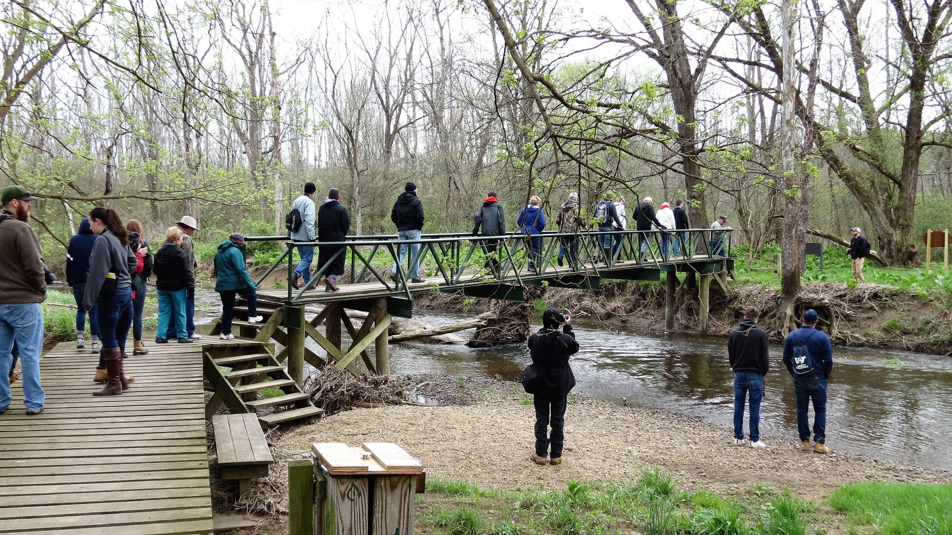 A group of people are standing on a wooden bridge over a river.