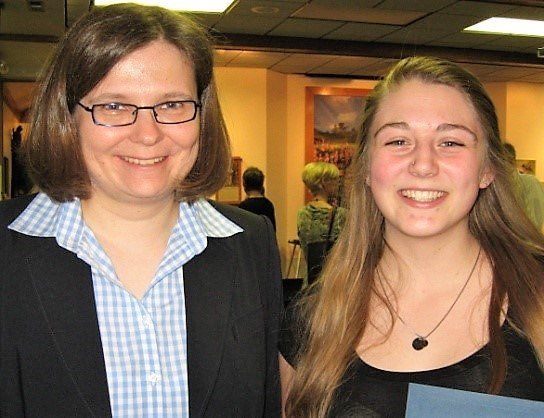A woman wearing glasses stands next to a young girl