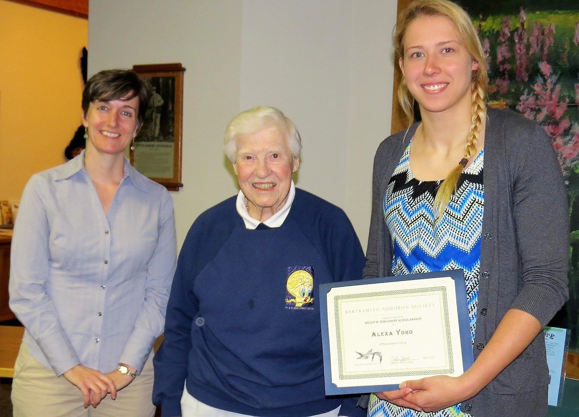A woman is holding a certificate in front of two other women