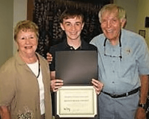 A young man is holding a certificate while standing next to two older people.