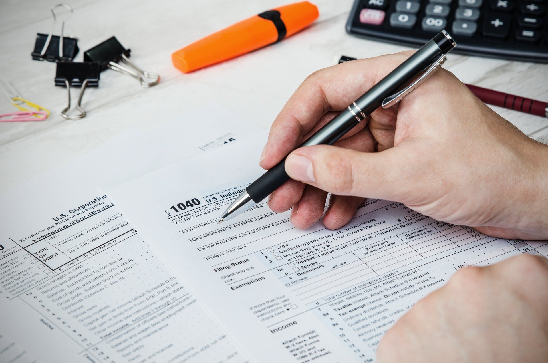 A person is writing on a tax form with a pen.