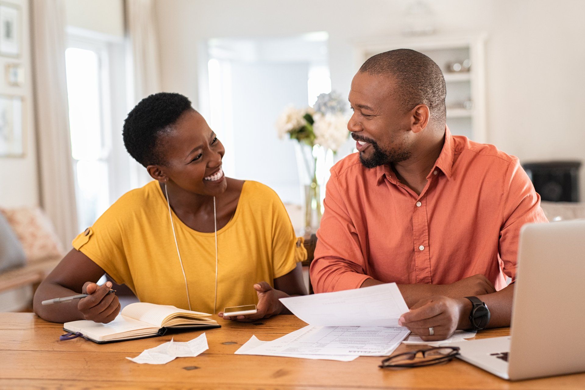 A man and a woman are sitting at a table with papers and a laptop.