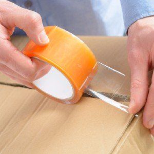 a person is holding a roll of tape over a cardboard box .