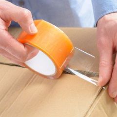 a person is holding a roll of tape over a cardboard box .