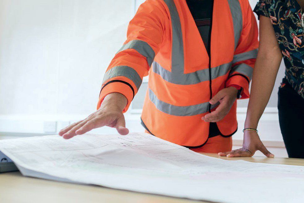 worker in fluorescent jacket looking at blueprints