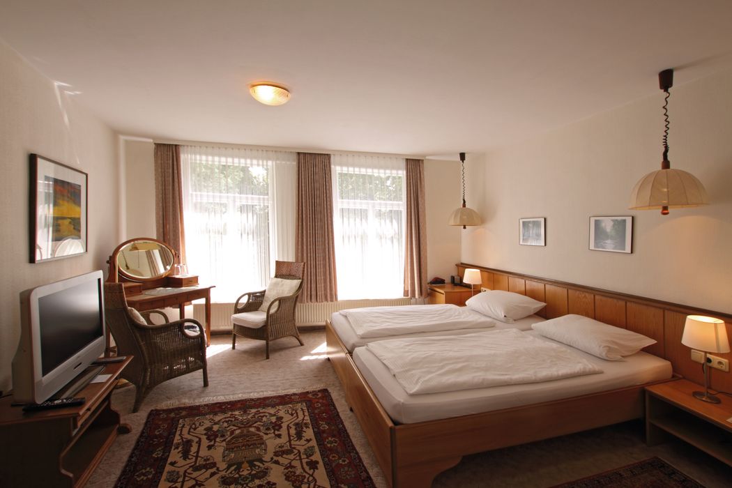 Ein Hotelzimmer mit zwei Betten, einem Sessel und einem Fernseher.