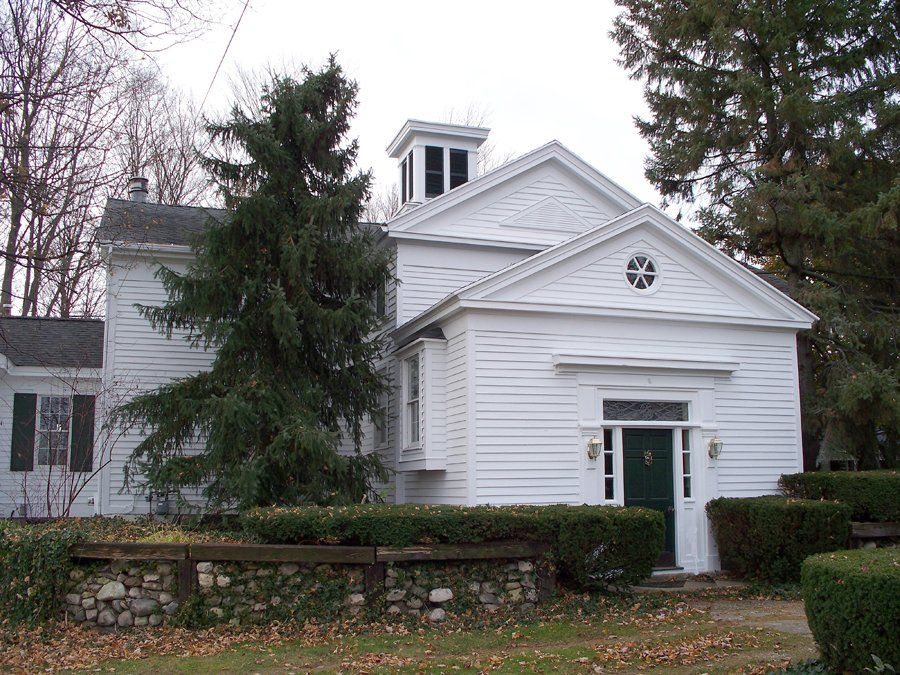 A white house with a green door is surrounded by trees