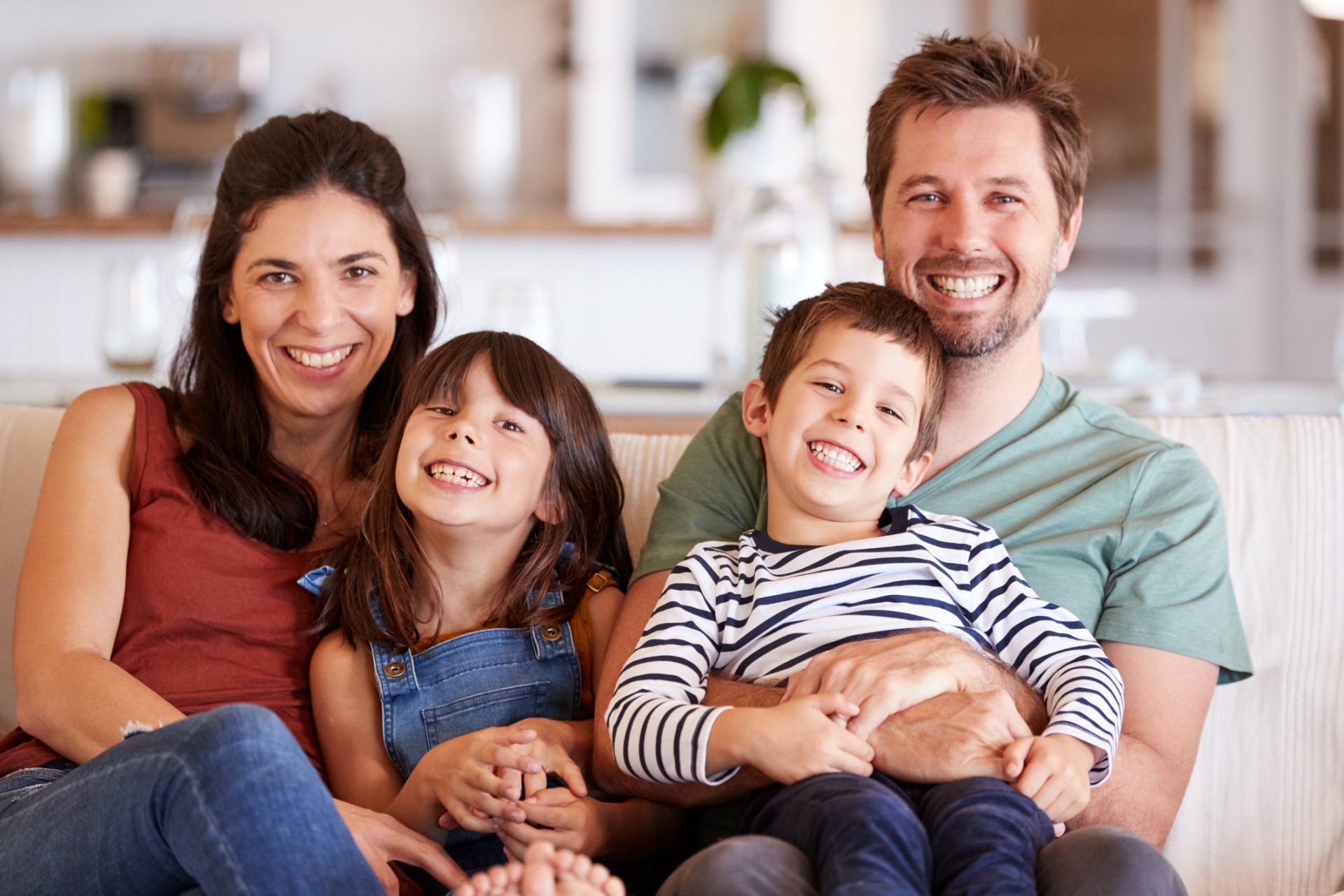 Family of four smiling on a couch indoors.