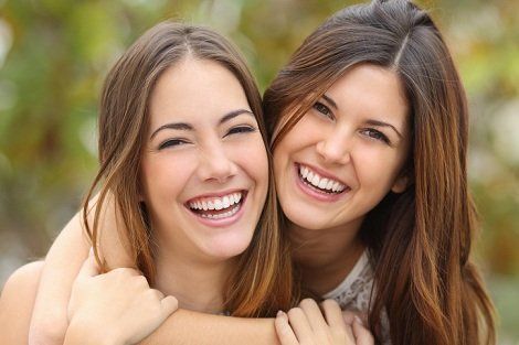 Two smiling people hugging outdoors.