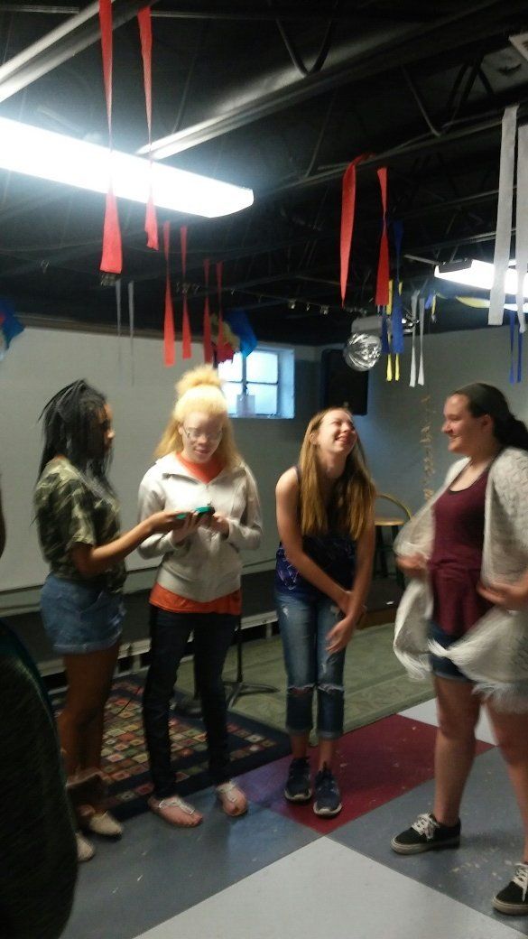 A group of young women are standing in a room with red flags hanging from the ceiling.