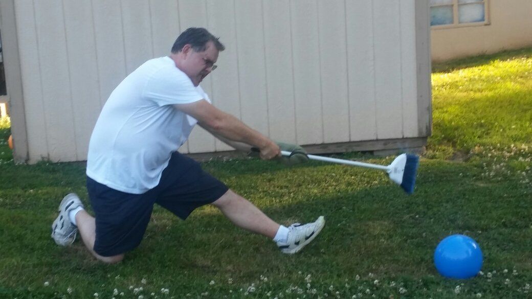 A man is kicking a ball with a broom