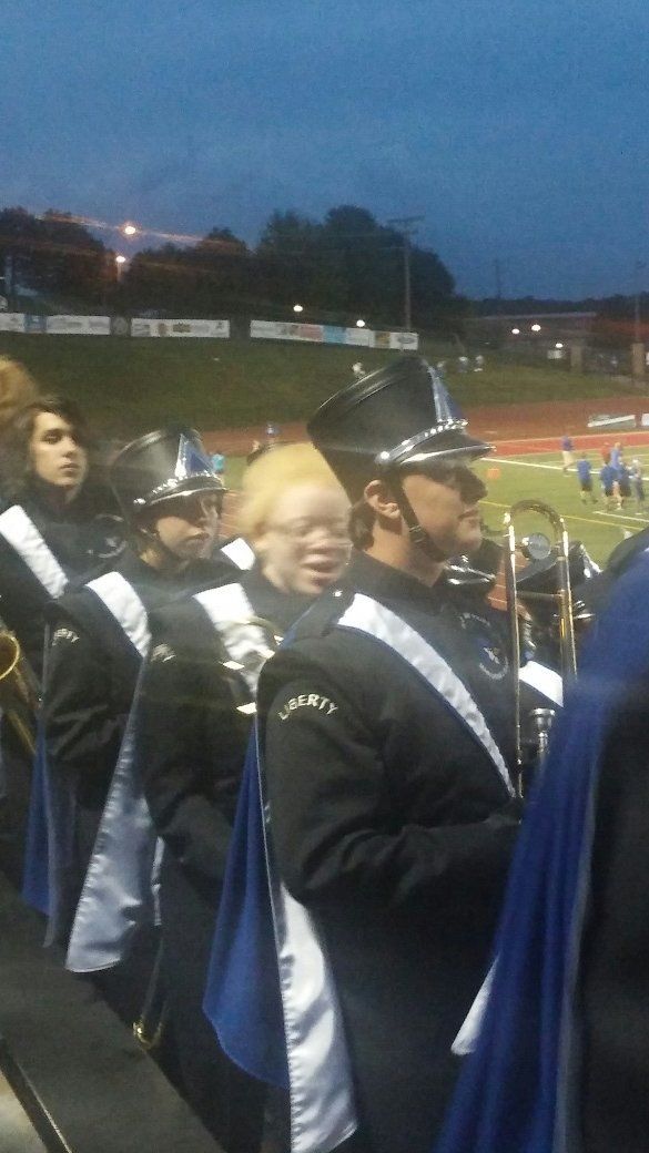 A group of marching band members are standing in a row on a field.