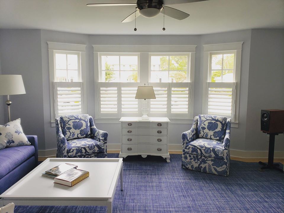 A blue and white living room with café shutters and floral-patterned chairs