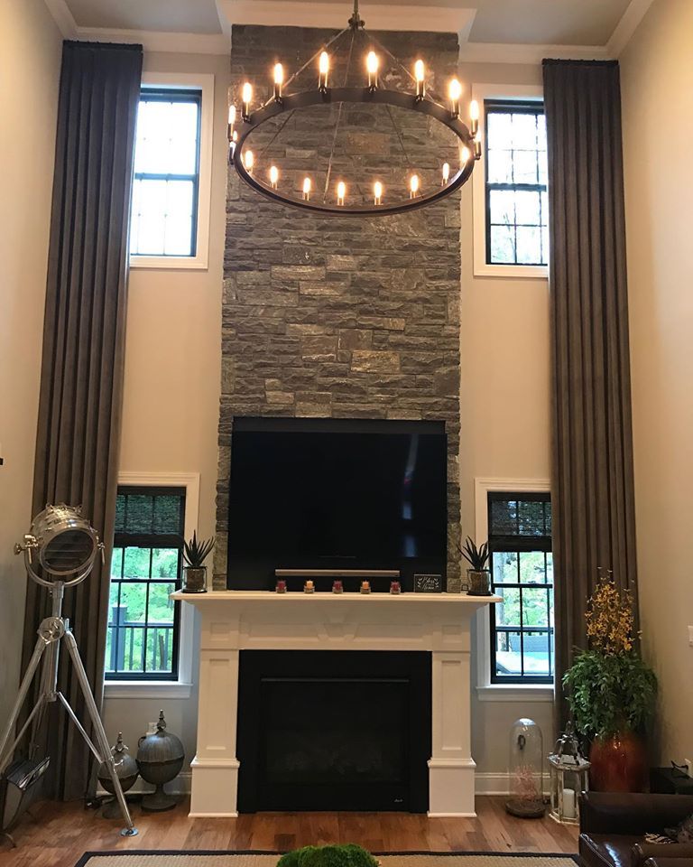  A tall open stone fireplace with mounted TV and drapery