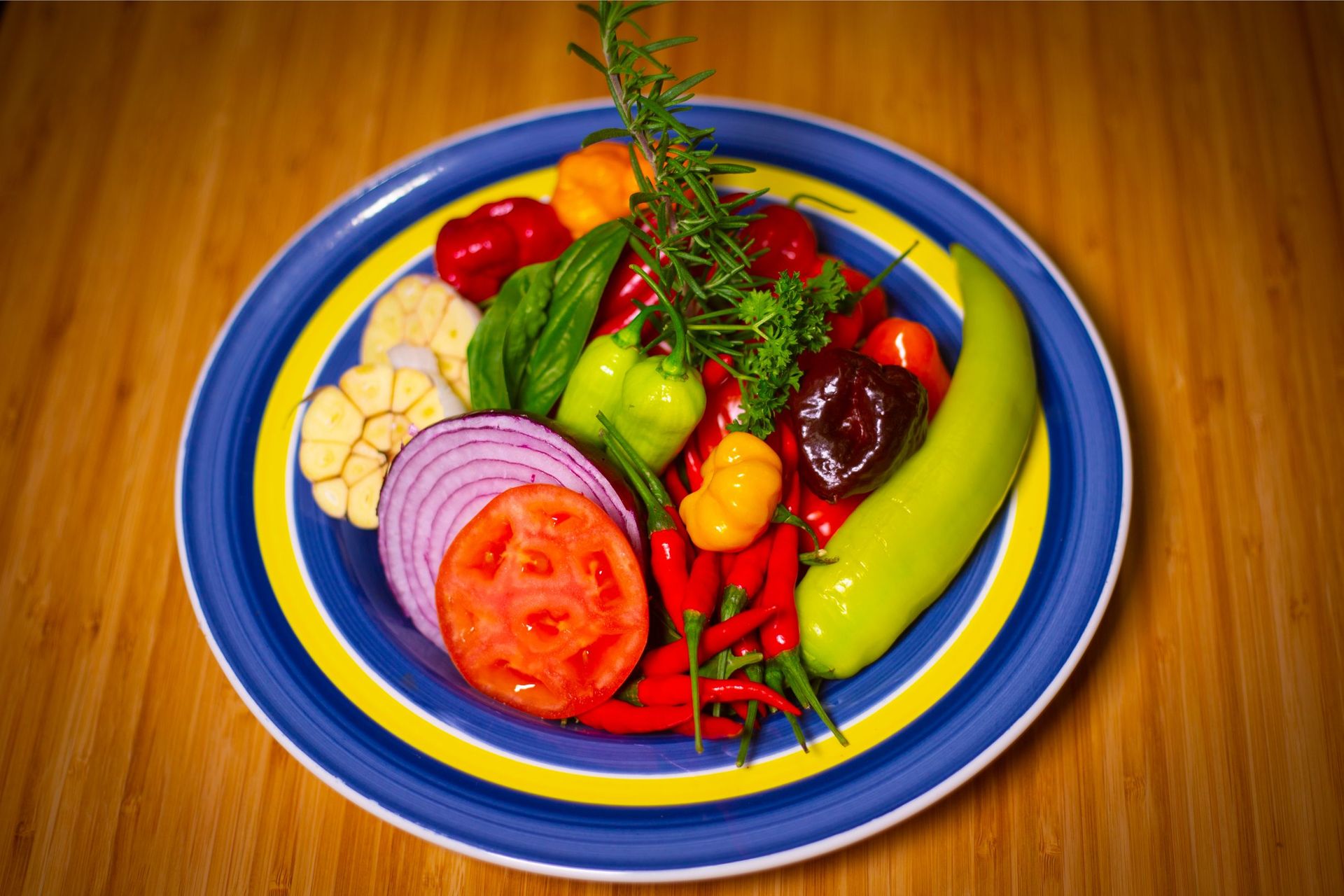 A blue and yellow plate topped with vegetables on a wooden table.