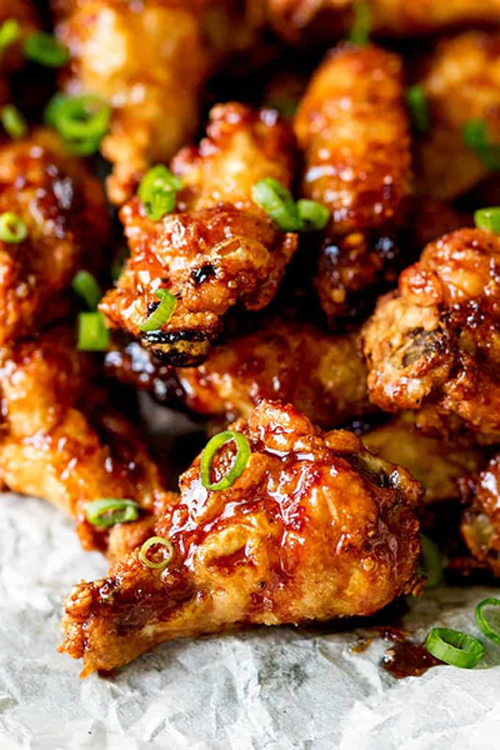 A close up of a pile of chicken wings with green onions on a table.