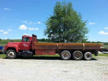 A red flatbed truck loaded with metal pipes, parked on a gravel lot under a clear blue sky.