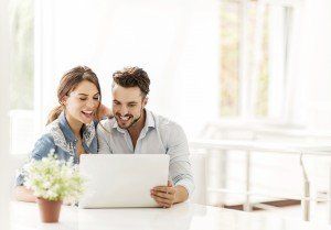 Smiling young couple sitting at home and using computer together.