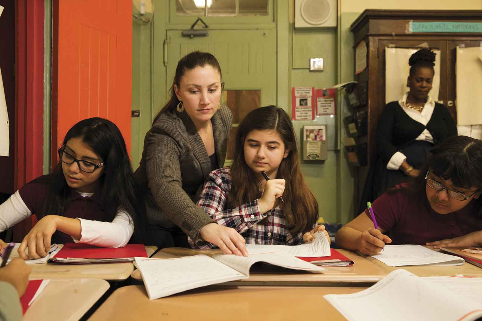 Multi ethnic classroom with female student working in notebooks and two female teachers helping them.