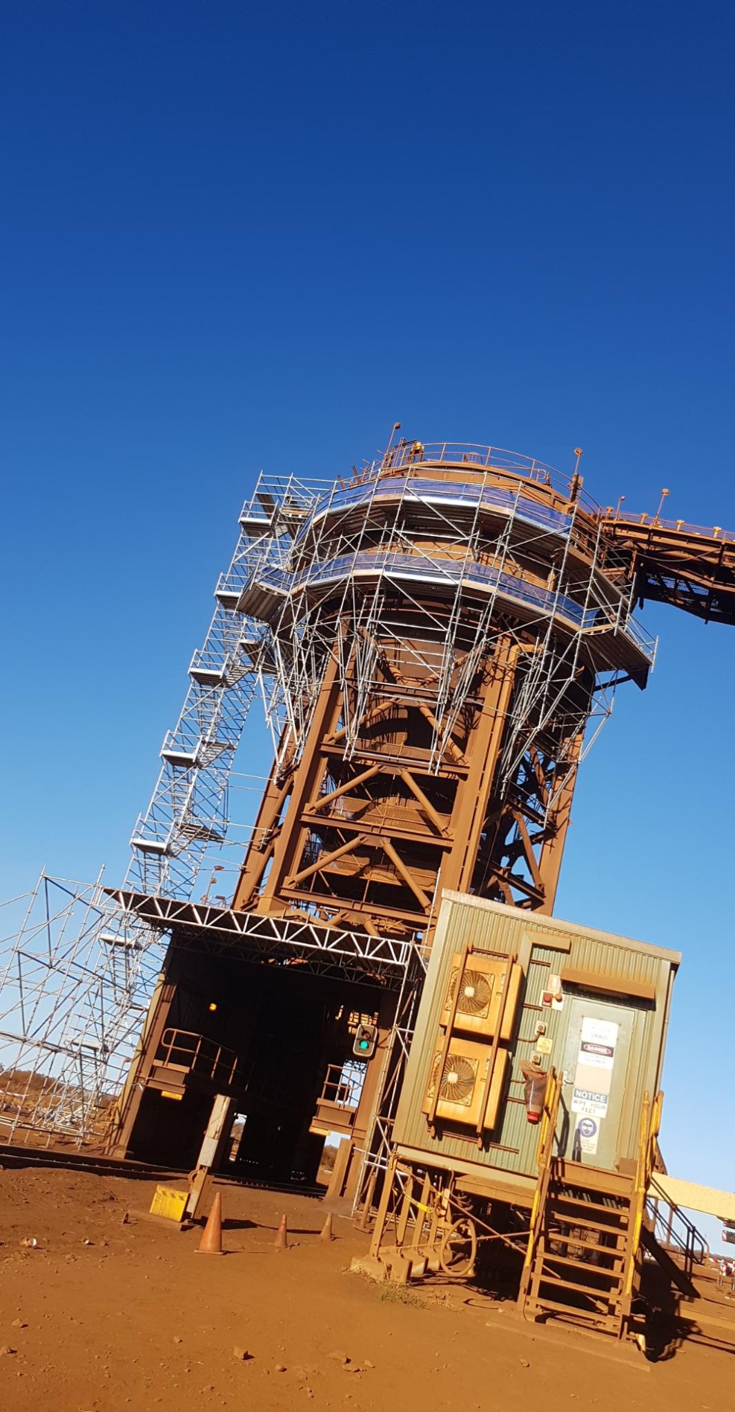 Tilted rust-colored industrial tower under construction against a clear blue sky