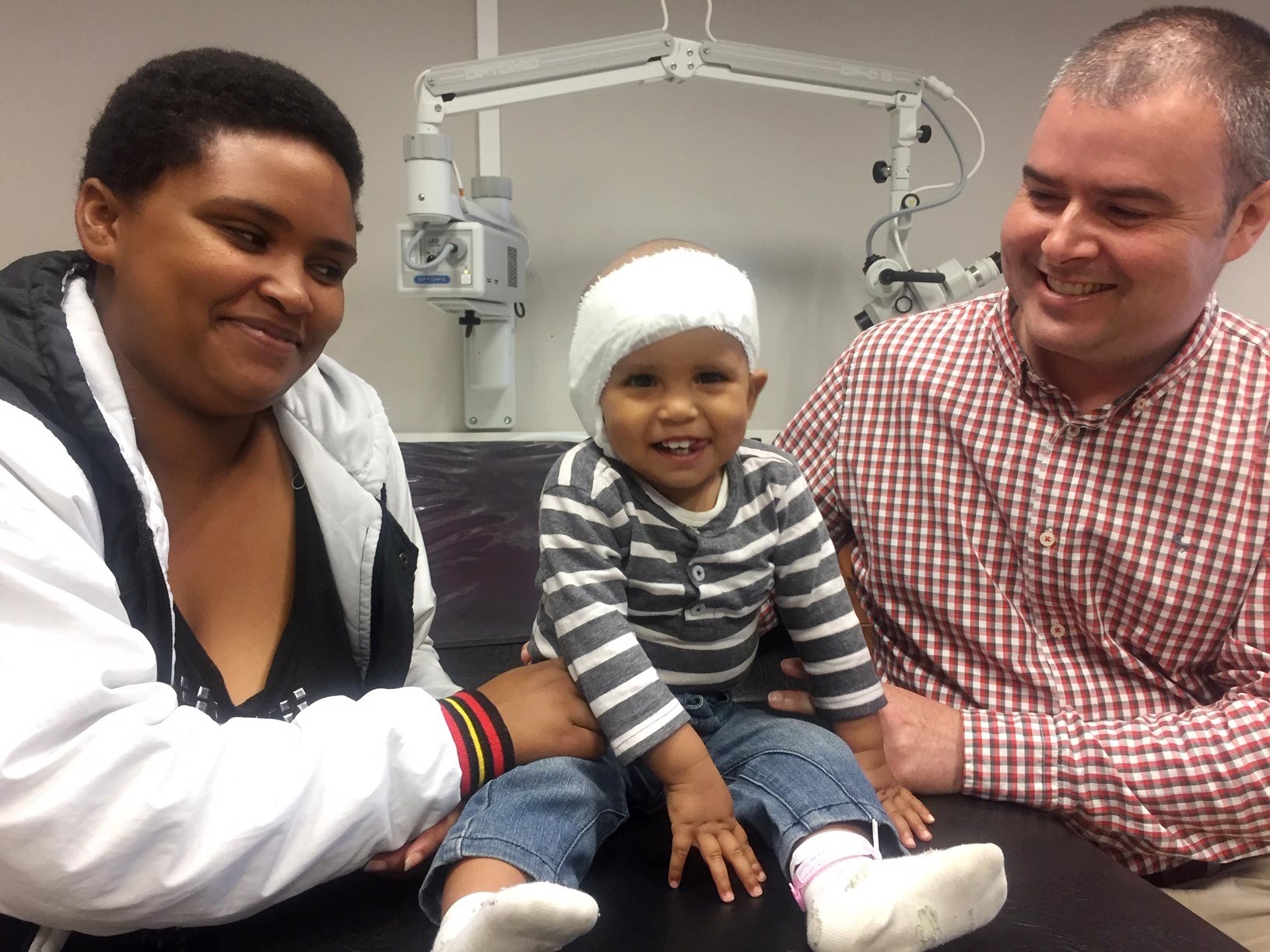 Brave 18-month-old Grayson Marais from Port Elizabeth (centre) pictured just prior to his bandages being removed at Netcare Greenacres Hospital. With Grayson is his mother Antoinette Marais (left), and Dr Iain Butler, the ear, nose and throat (ENT) specialist who performed the cochlear implant. Brave 18-month-old Grayson Marais from Port Elizabeth (centre) pictured just prior to his bandages being removed at Netcare Greenacres Hospital. With Grayson is his mother Antoinette Marais (left), and Dr Iain Butler, the ear, nose and throat (ENT) specialist who performed the cochlear implant.