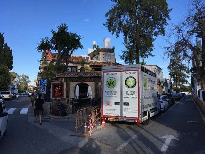 A delivery truck is parked on a narrow street with a restaurant, people, and cars.