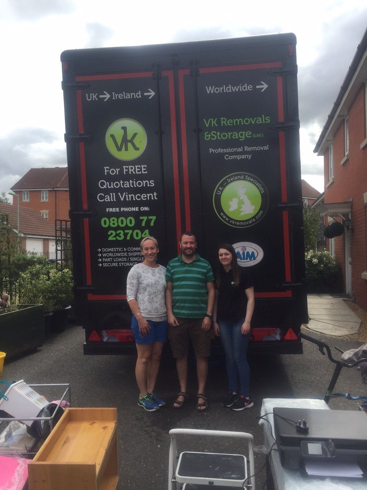 Three people stand in front of a black removal truck. The truck has the VK Removals logo.