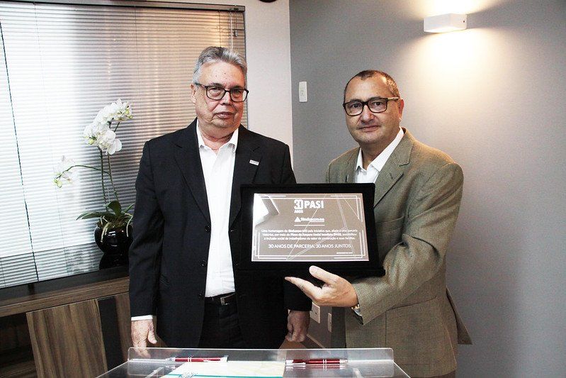 Dois homens estão de pé, um ao lado do outro, segurando uma placa.