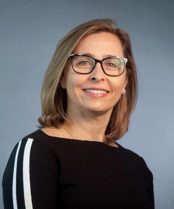 Uma mulher usando óculos e uma camisa preta está sorrindo para a câmera.