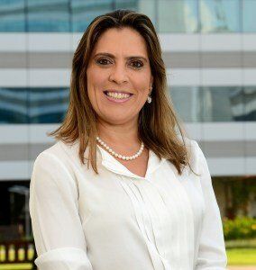 Uma mulher de camisa branca e colar de pérolas está sorrindo em frente a um prédio.