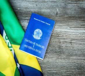 Um passaporte azul está sobre uma bandeira brasileira em uma mesa de madeira.