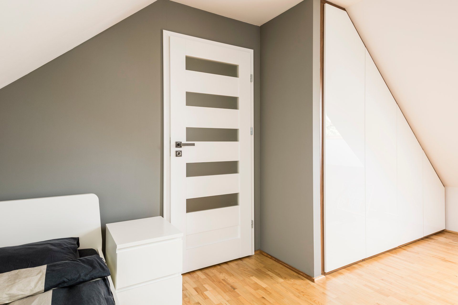 A bedroom with a slanted ceiling and a white door.