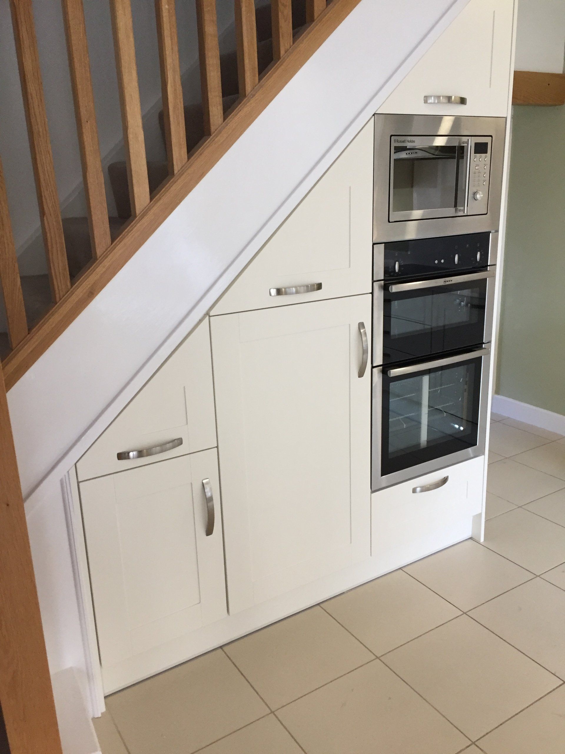 A kitchen with a microwave oven under the stairs