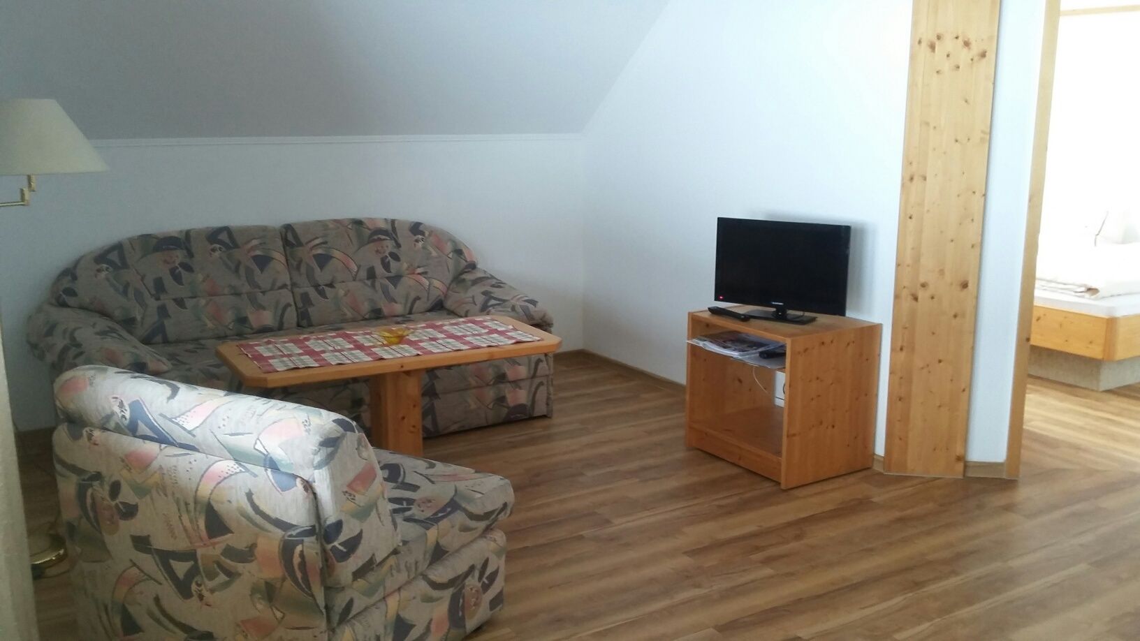 Ein Wohnzimmer mit Couch, Sessel, Tisch und Fernseher.