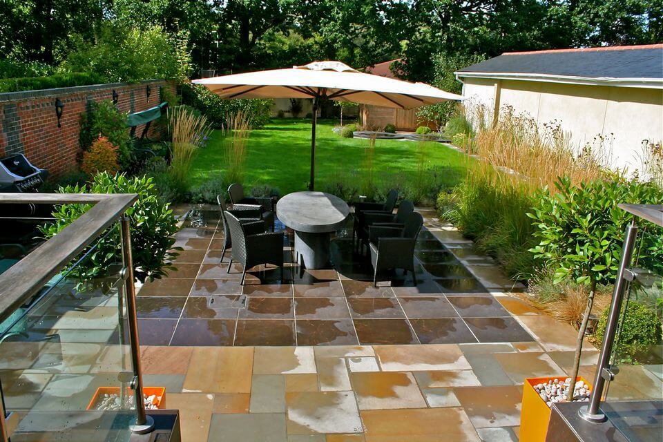 table and chairs under an umbrella in a garden after rain