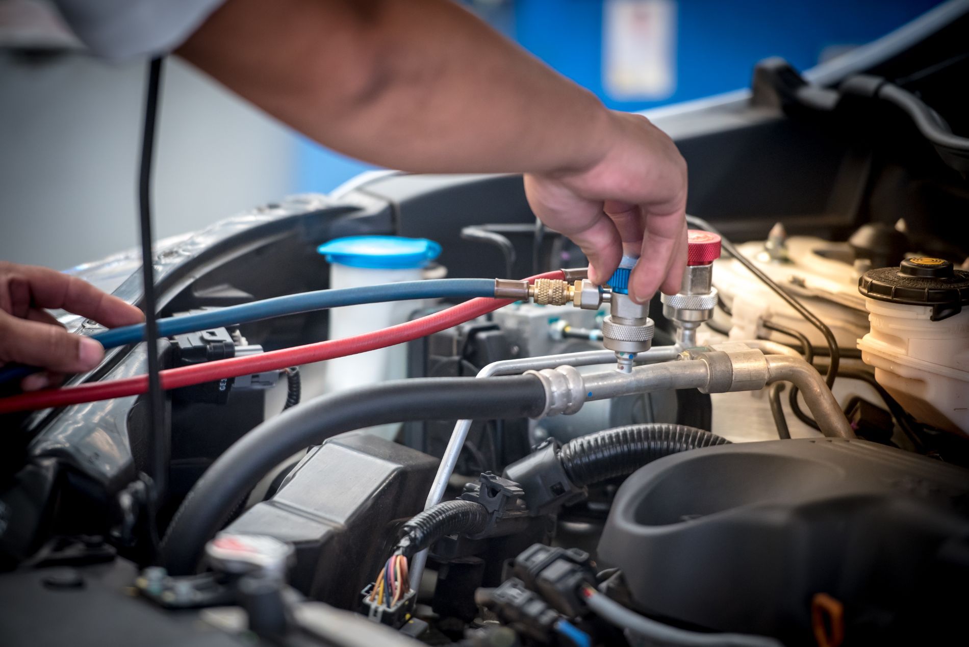 Technician connecting A/C recharge hoses to a car engine, auto air conditioning service in Cincinnati, OH