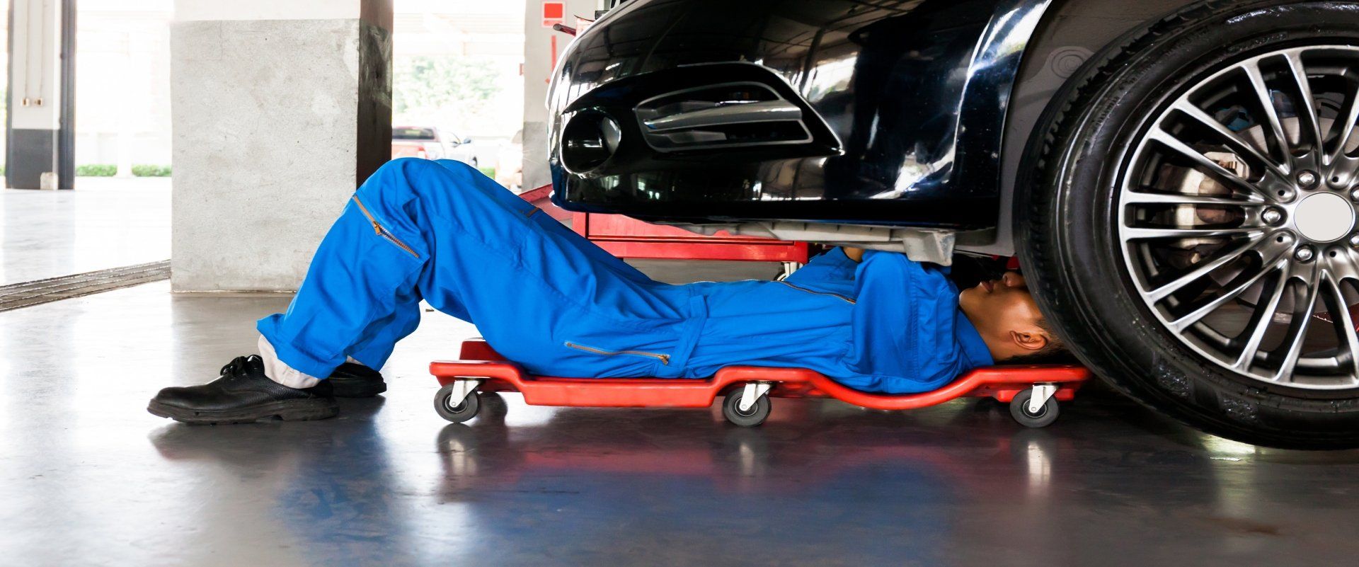 Mechanic in blue uniform working under a vehicle on a creeper, auto repair in Cincinnati, OH