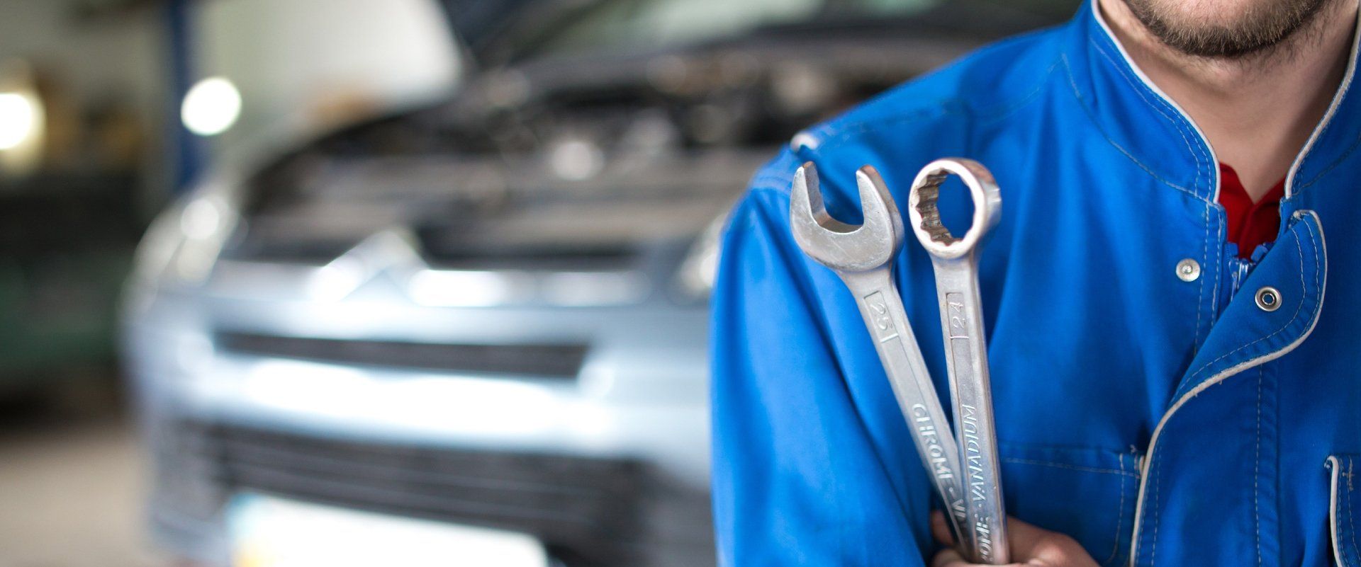 Mechanic in blue uniform holding wrenches, auto repair and tire service in Cincinnati, OH