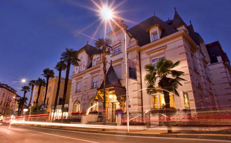 Un grande edificio con palme davanti è illuminato di notte.