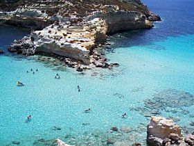 Un gruppo di persone sta nuotando nel mare del Salento vicino a una costa rocciosa