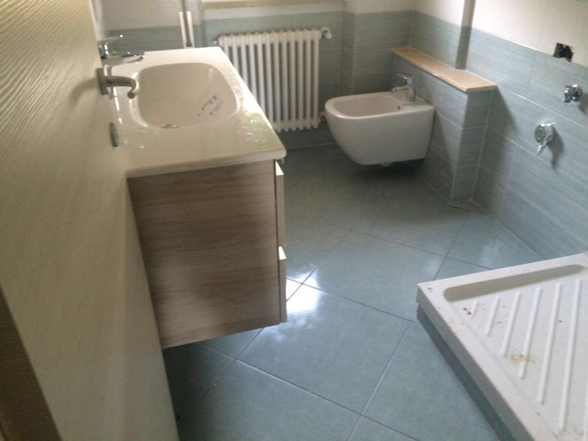 Bagno con pareti e pavimento piastrellati blu; comprende lavandino, bidet, termosifone e piatto doccia.
