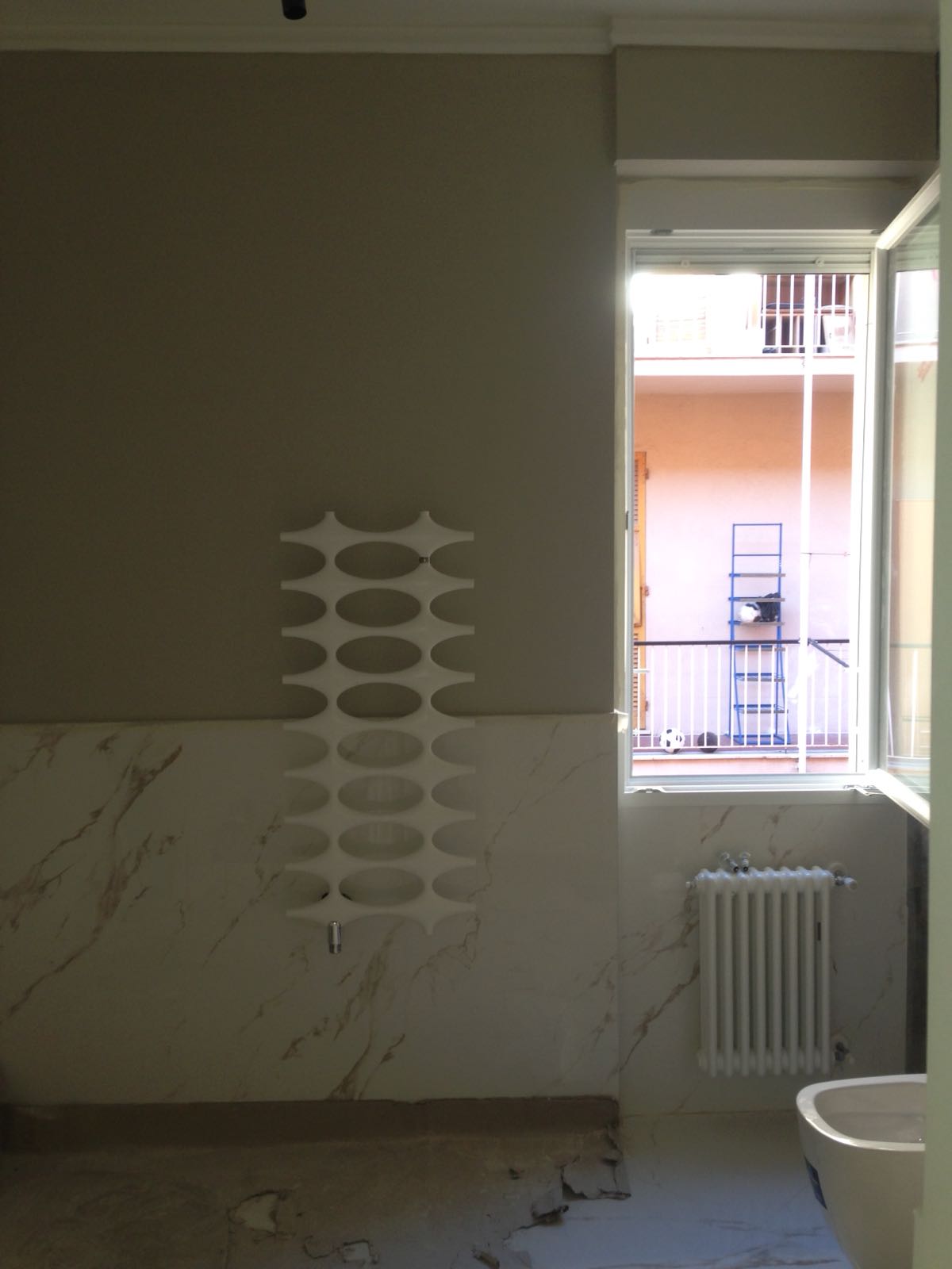 Bagno con parete grigia, rivestimento in marmo, termosifone decorativo, finestra aperta sul balcone.