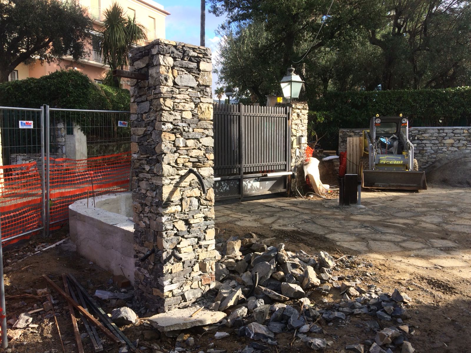 Cantiere con colonne in pietra, cancello e abbeveratoio.