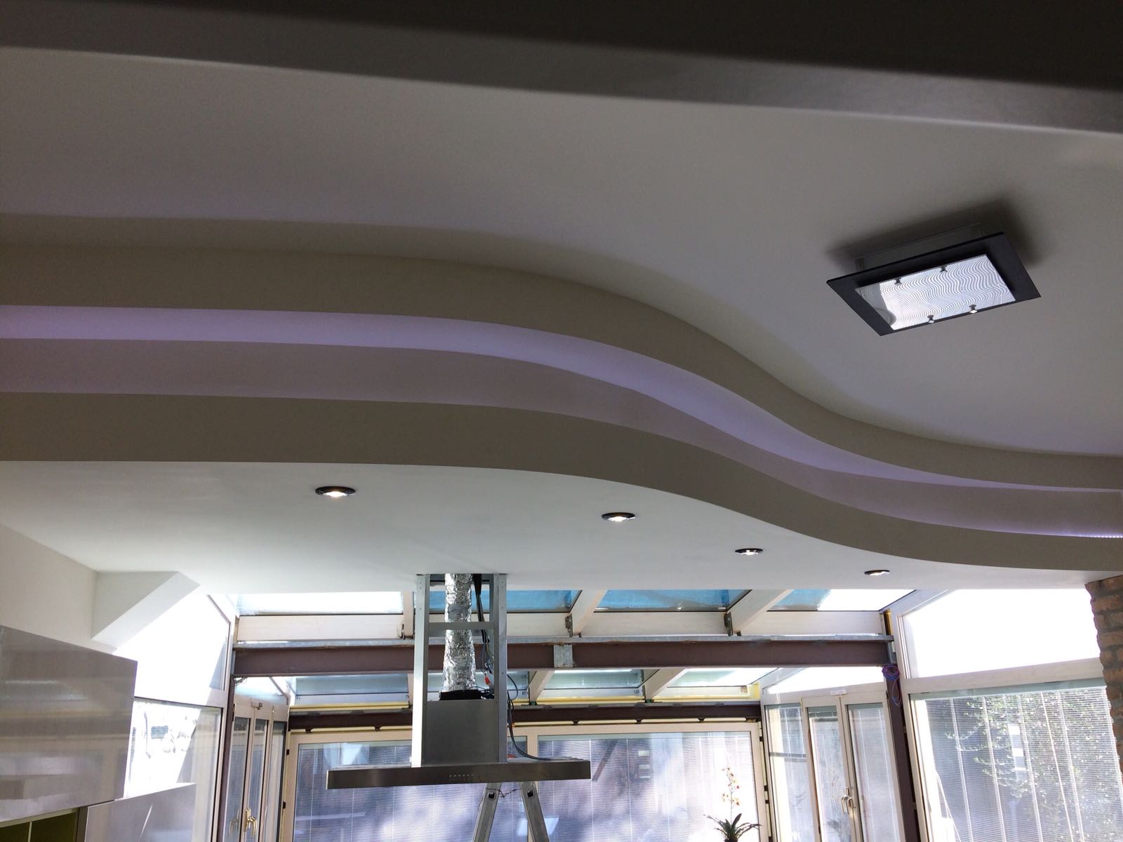 Moderno soffitto da cucina con luci da incasso, design ondulato e lampadario rettangolare.