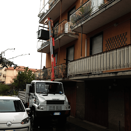 Camion con piattaforma elevatrice accanto all'edificio. Una persona è sulla piattaforma e lavora sui balconi.