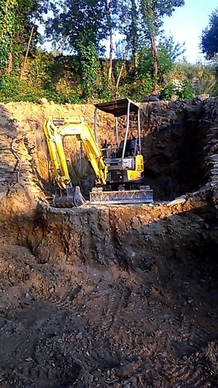 Escavatore giallo in una buca profonda, che scava nel terreno. Cantiere, all'aperto, soleggiato.