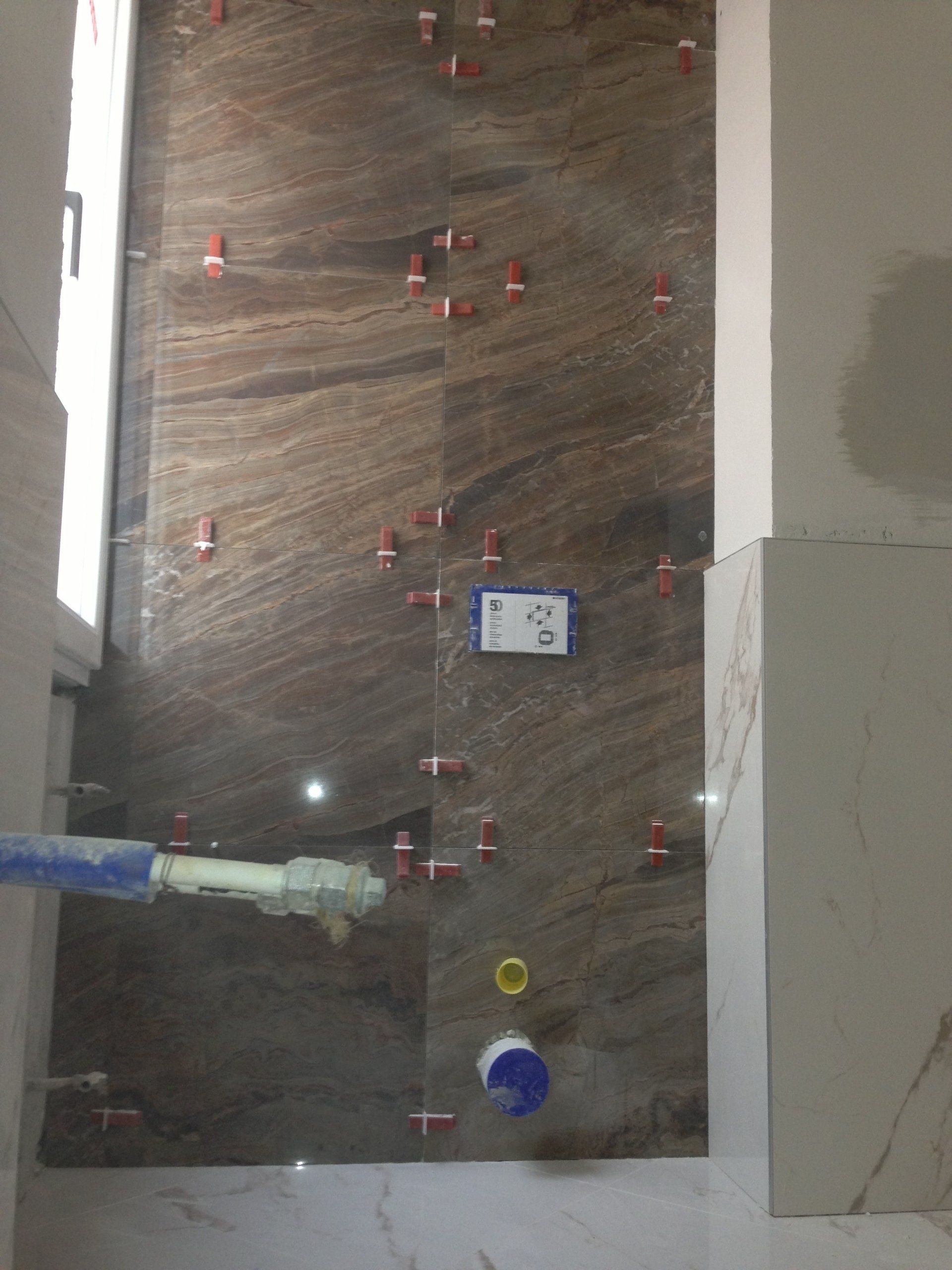 Piastrelle installate su una parete del bagno, con distanziatori di livellamento. Sono visibili gli impianti idraulici.