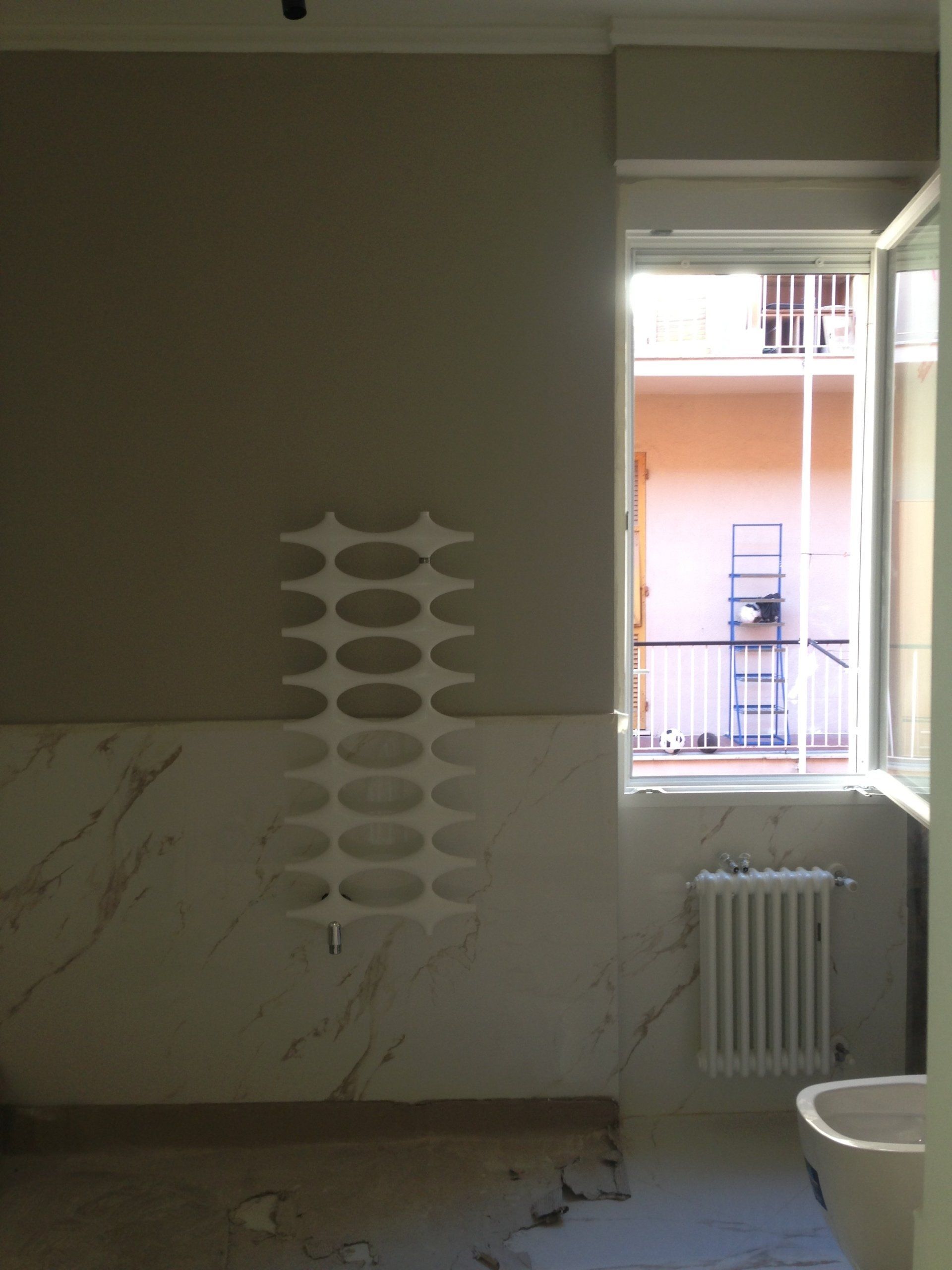Vista interna di una stanza con un elemento decorativo bianco a parete. Finestra aperta, pareti beige e marmo.