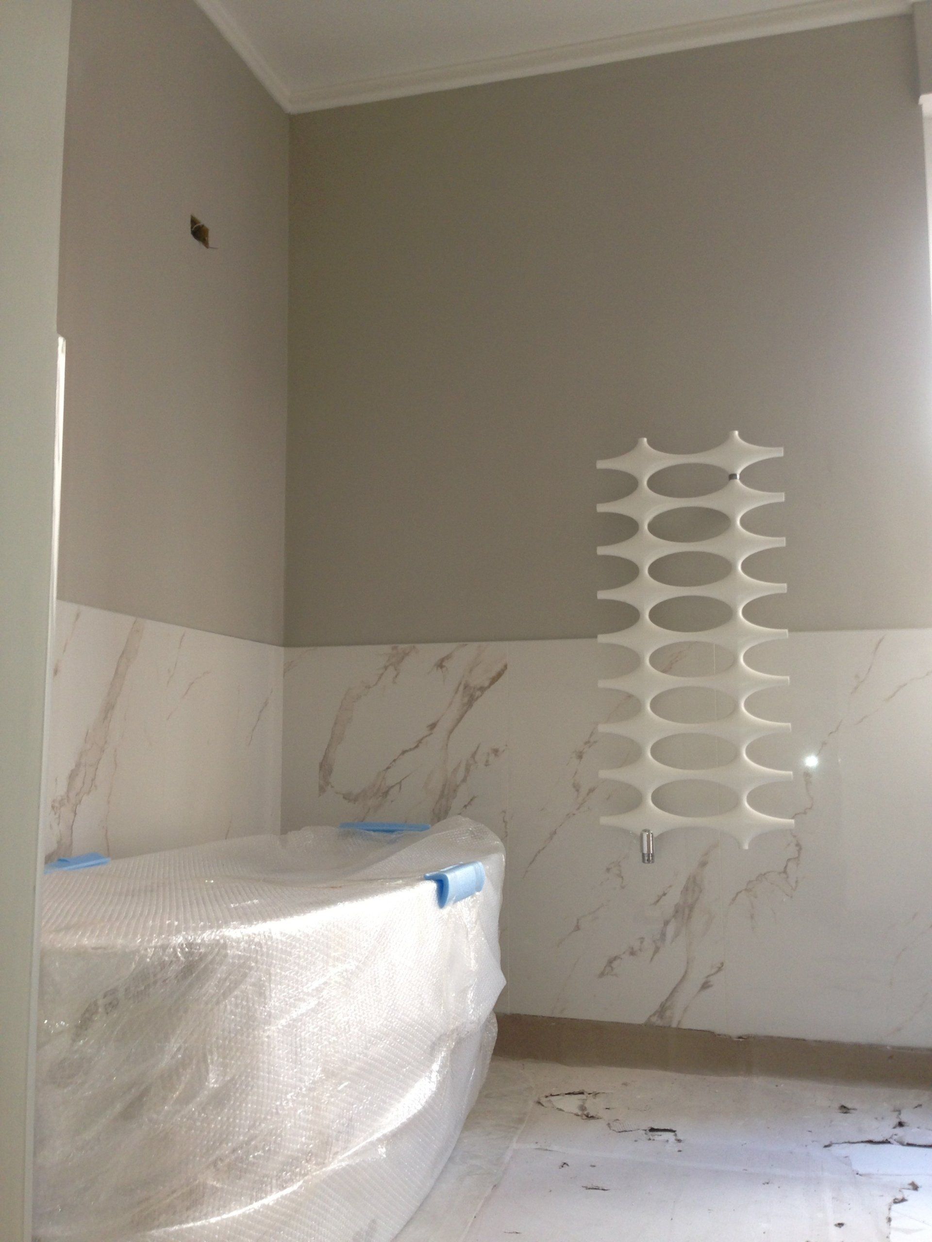 Bagno in costruzione, con vasca rivestita e un radiatore unico a parete. Pareti in marmo e grigio.